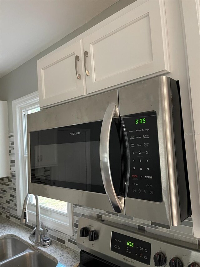 room details featuring sink, white cabinets, and decorative backsplash