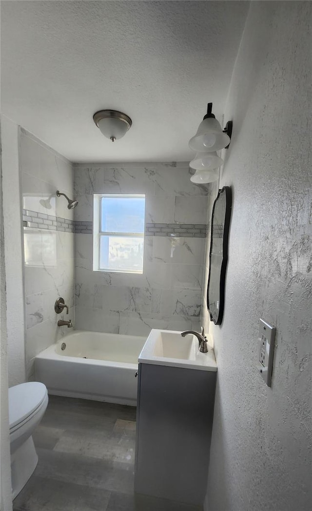 full bathroom with a textured ceiling, toilet, vanity, and tiled shower / bath