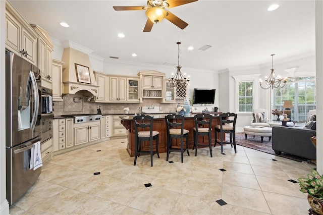 kitchen with custom range hood, ceiling fan with notable chandelier, cream cabinetry, stainless steel appliances, and decorative backsplash