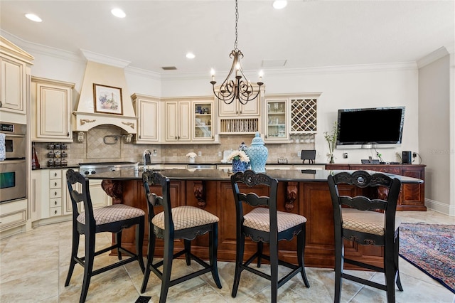 kitchen featuring a breakfast bar, a kitchen island with sink, decorative light fixtures, cream cabinetry, and stainless steel double oven