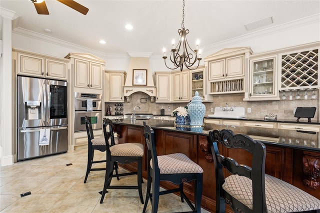 kitchen with stainless steel appliances, cream cabinetry, pendant lighting, ceiling fan with notable chandelier, and backsplash