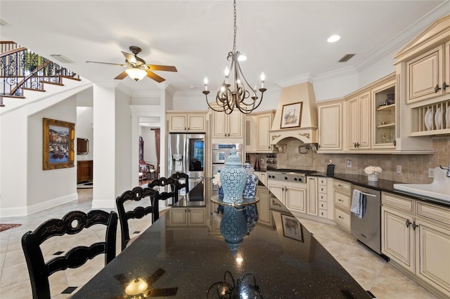 kitchen featuring appliances with stainless steel finishes, premium range hood, light tile patterned floors, ceiling fan with notable chandelier, and cream cabinets