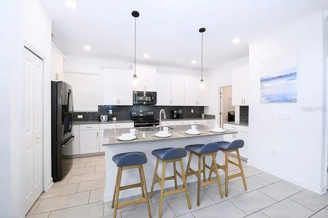 kitchen with white cabinetry, a center island with sink, a breakfast bar area, pendant lighting, and black appliances