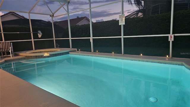 pool at dusk with a lanai and an in ground hot tub