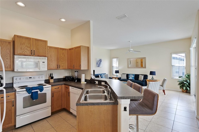 kitchen featuring a breakfast bar, sink, light tile patterned floors, kitchen peninsula, and white appliances