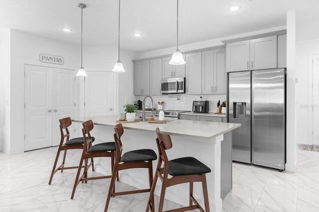 kitchen featuring gray cabinetry, stainless steel appliances, pendant lighting, a center island with sink, and a breakfast bar area