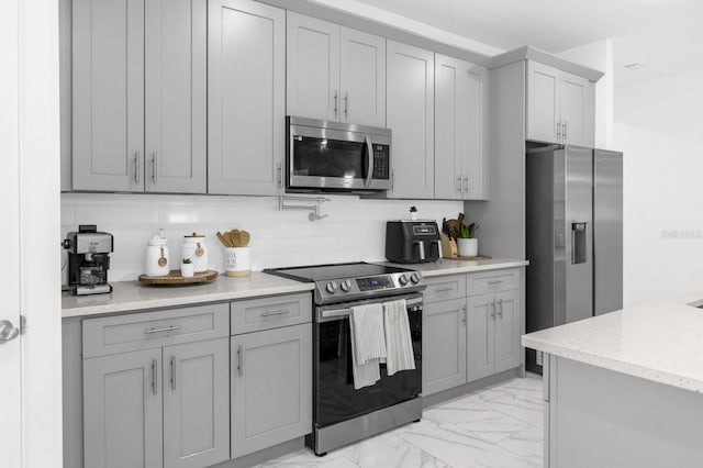 kitchen with decorative backsplash, stainless steel appliances, light stone countertops, and gray cabinetry