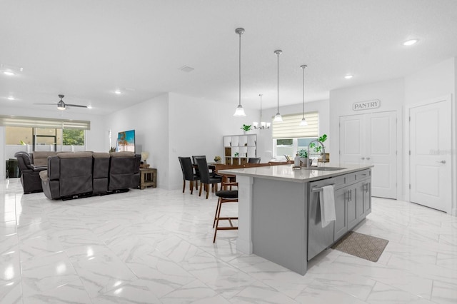 kitchen featuring ceiling fan with notable chandelier, sink, pendant lighting, gray cabinets, and an island with sink