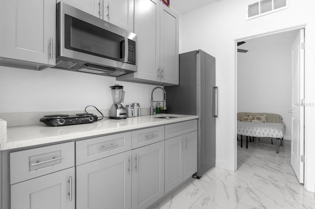 kitchen with gray cabinetry, refrigerator, light stone countertops, and sink