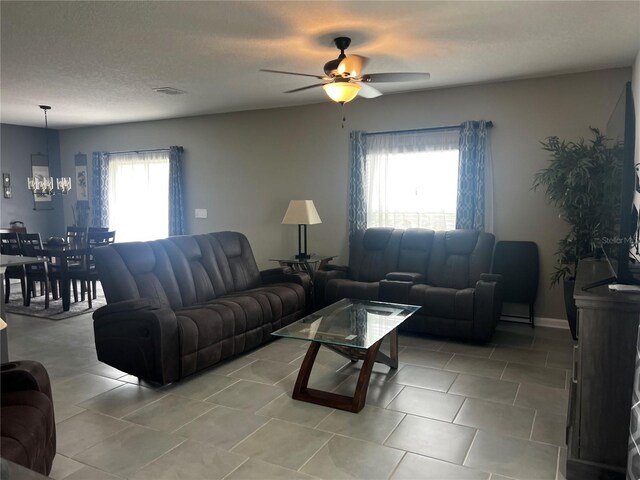 living room with a textured ceiling, a healthy amount of sunlight, and ceiling fan with notable chandelier