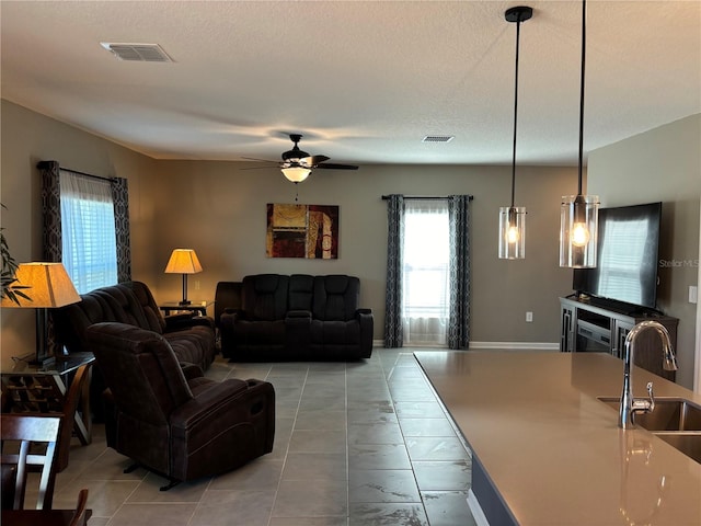 living room with ceiling fan, light tile patterned floors, a textured ceiling, and sink