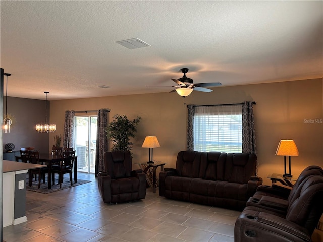 living room with ceiling fan with notable chandelier, a textured ceiling, and light tile patterned floors