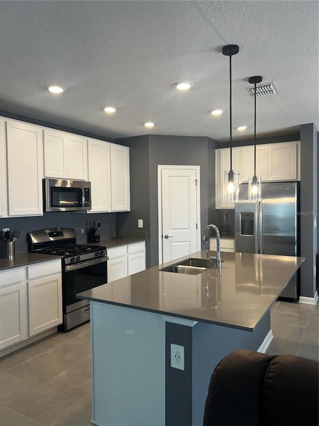 kitchen featuring pendant lighting, a textured ceiling, sink, appliances with stainless steel finishes, and a center island with sink