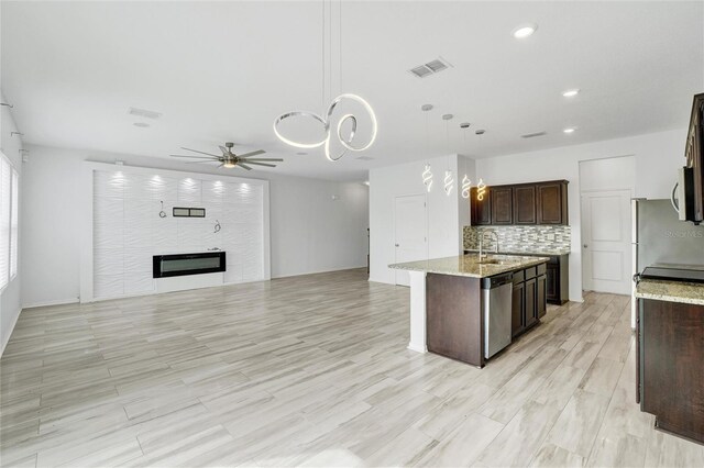 kitchen with stainless steel appliances, dark brown cabinets, pendant lighting, an island with sink, and light hardwood / wood-style flooring