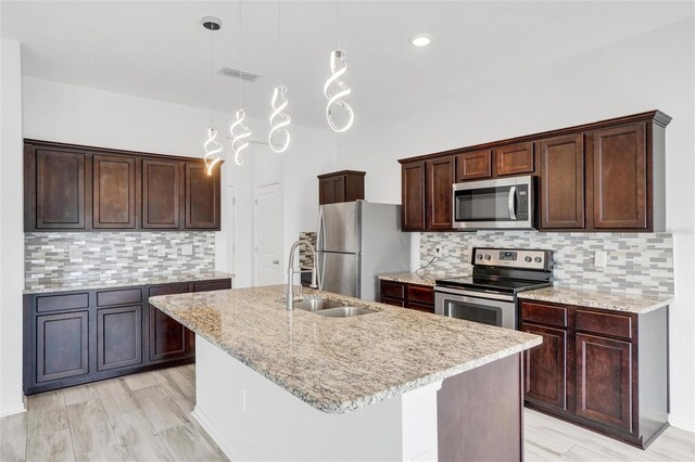 kitchen with sink, appliances with stainless steel finishes, decorative light fixtures, an island with sink, and light wood-type flooring