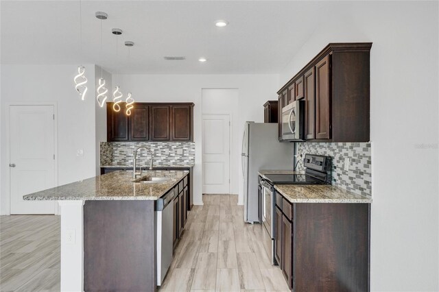 kitchen featuring decorative backsplash, sink, light stone countertops, pendant lighting, and appliances with stainless steel finishes