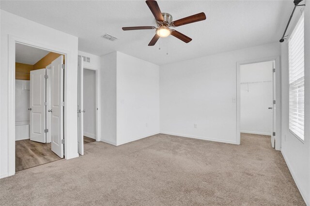 unfurnished bedroom with ceiling fan, light carpet, a closet, and a walk in closet