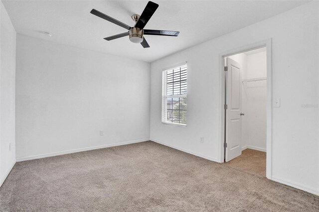 unfurnished bedroom with ceiling fan, a closet, a walk in closet, and light colored carpet