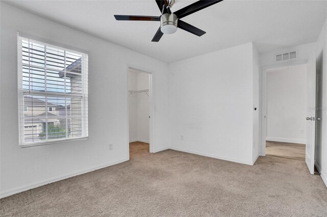 unfurnished bedroom with a closet, a spacious closet, light colored carpet, and ceiling fan