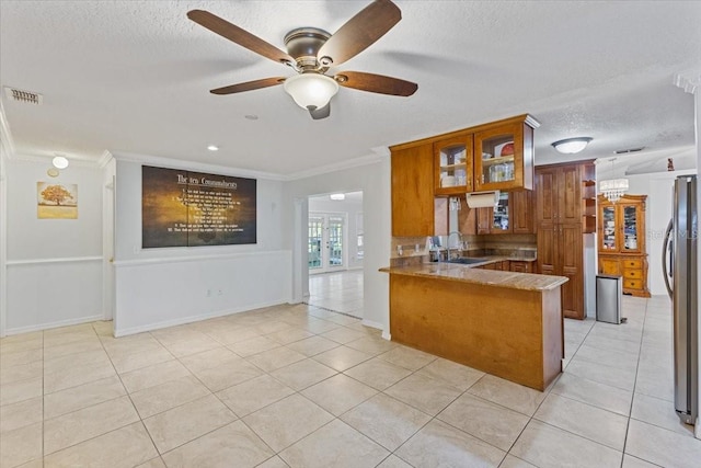 kitchen featuring light tile patterned floors, crown molding, stainless steel fridge, and kitchen peninsula