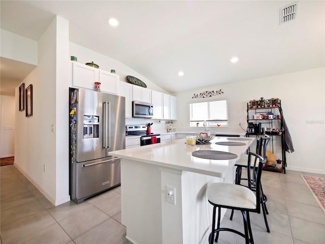 kitchen with appliances with stainless steel finishes, lofted ceiling, a kitchen island, white cabinets, and a breakfast bar