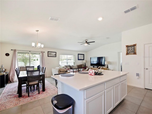 kitchen with decorative light fixtures, vaulted ceiling, a kitchen island, white cabinets, and ceiling fan with notable chandelier