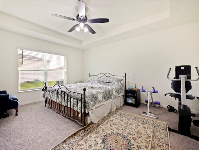 carpeted bedroom with ceiling fan and a raised ceiling