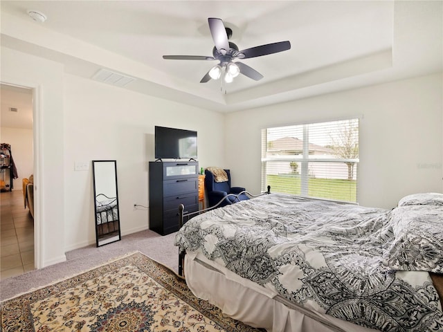 bedroom with light carpet, ceiling fan, and a tray ceiling