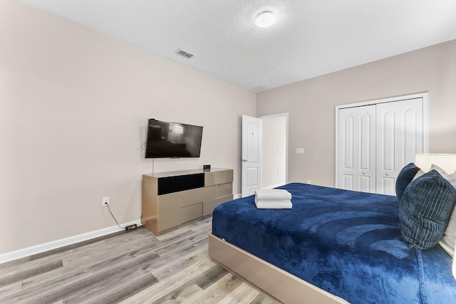 bedroom with light hardwood / wood-style floors, a textured ceiling, and a closet