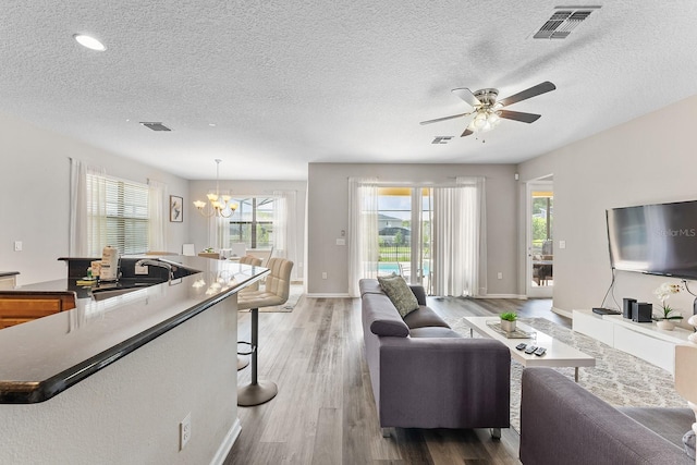 living room with ceiling fan with notable chandelier, wood-type flooring, sink, and a textured ceiling