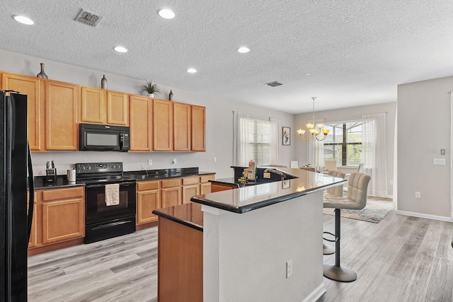 kitchen featuring light wood-type flooring, a textured ceiling, black appliances, pendant lighting, and a center island with sink