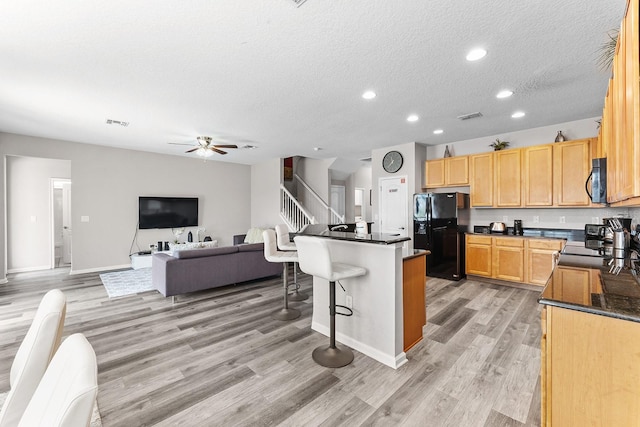 kitchen featuring a breakfast bar, a center island, ceiling fan, light hardwood / wood-style floors, and black appliances