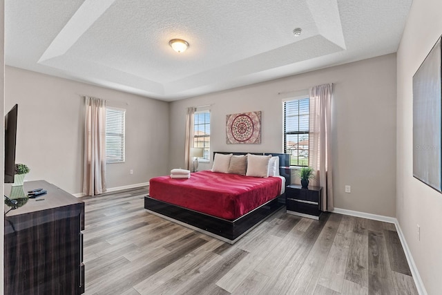 bedroom with a textured ceiling, wood-type flooring, and a tray ceiling