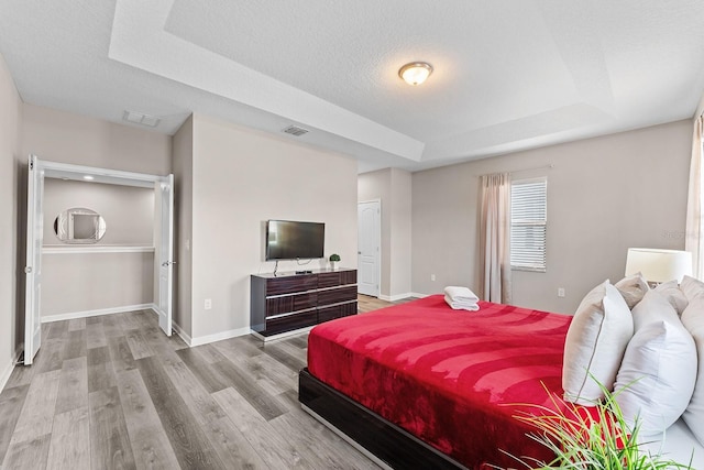 bedroom with light hardwood / wood-style floors, a raised ceiling, and a textured ceiling