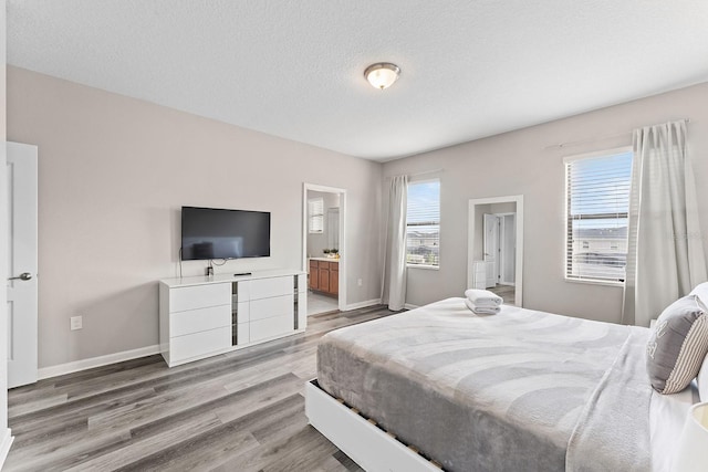 bedroom with ensuite bathroom, a textured ceiling, and light hardwood / wood-style flooring