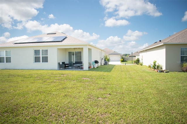 back of property with a garage, a yard, a patio area, and solar panels