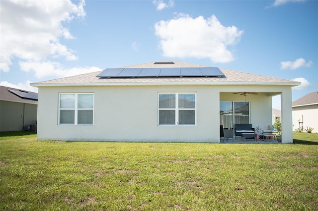 rear view of property featuring ceiling fan, a lawn, and solar panels