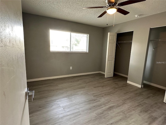 unfurnished bedroom featuring multiple closets, ceiling fan, hardwood / wood-style floors, and a textured ceiling