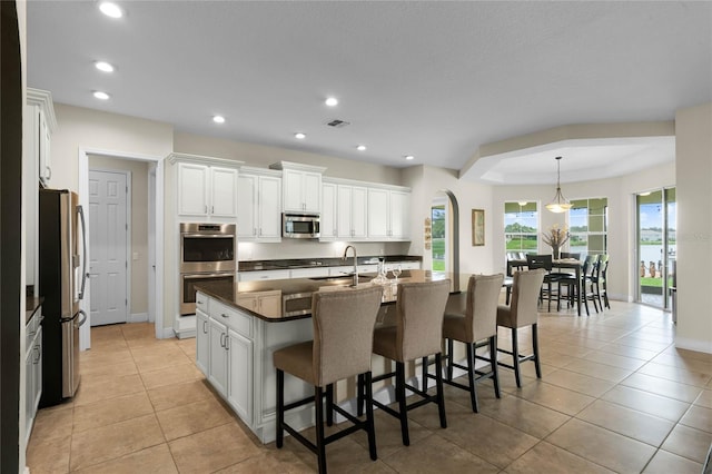 kitchen featuring hanging light fixtures, a kitchen island with sink, a breakfast bar area, stainless steel appliances, and white cabinets