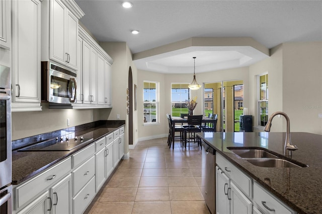 kitchen with white cabinetry, stainless steel appliances, dark stone countertops, sink, and a raised ceiling