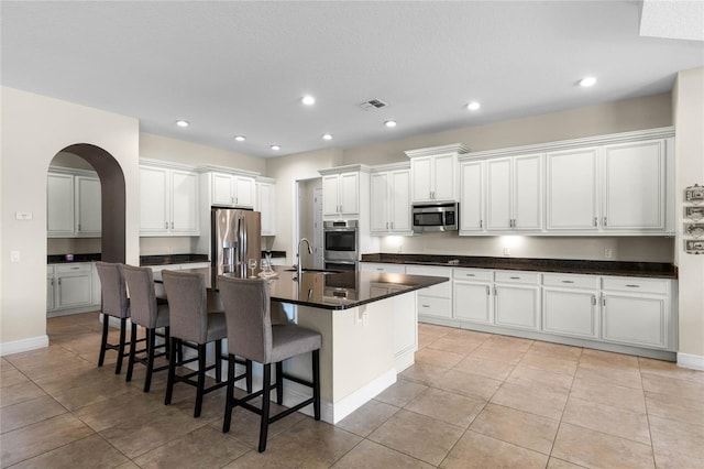 kitchen featuring appliances with stainless steel finishes, a kitchen bar, white cabinetry, light tile patterned floors, and a center island with sink