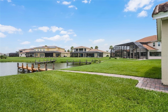 view of dock with a water view, a lawn, and glass enclosure