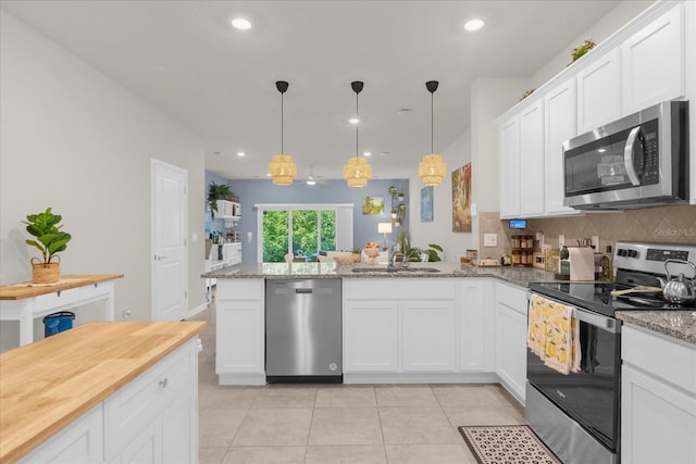 kitchen with stainless steel appliances, light tile patterned flooring, a sink, white cabinetry, and a peninsula