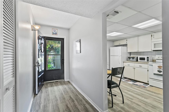 kitchen with backsplash, white cabinets, white appliances, a drop ceiling, and light wood-type flooring