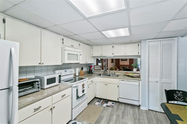 kitchen with white cabinetry, sink, decorative backsplash, white appliances, and light hardwood / wood-style flooring