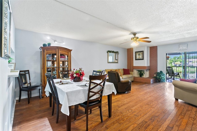 dining area featuring wood-type flooring, ceiling fan, a textured ceiling, and a fireplace