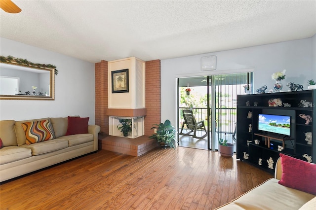 living room featuring a brick fireplace, a textured ceiling, wood-type flooring, and ceiling fan