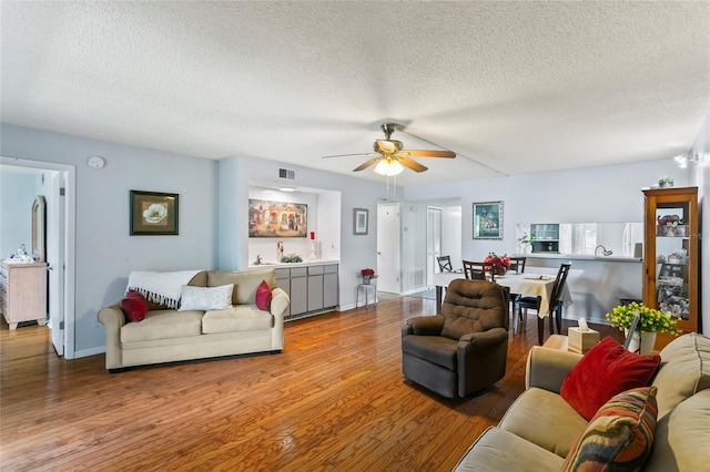 living room with ceiling fan, wood-type flooring, and a textured ceiling