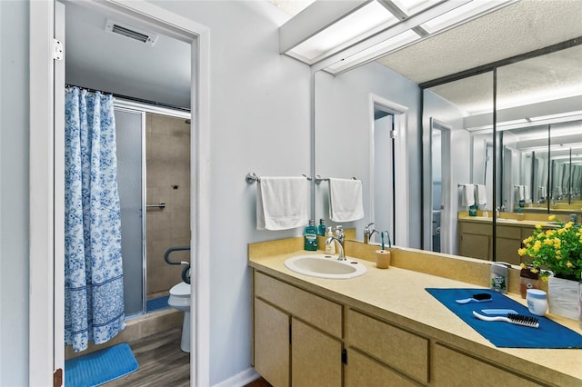 bathroom with wood-type flooring, vanity, an enclosed shower, toilet, and a textured ceiling