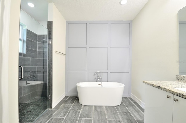 bathroom with a textured ceiling, vanity, and shower with separate bathtub